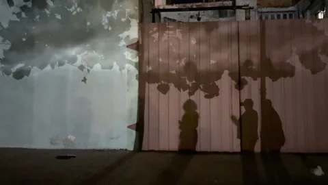 People's shadows are projected onto a wall with a cloudy Stock Footage 312896747