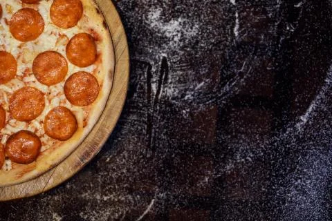 Pepperoni pizza in the left corner, focus on it. Black background, copy space. Stock Photos