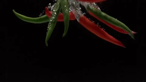 Peppers fall into water in slow motion. on a black background Stock Footage 131037124