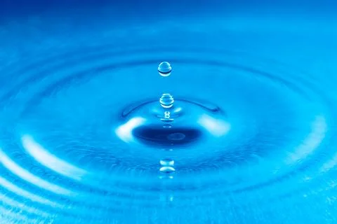 Perfectly captured water drop creating ripples on a vibrant blue surface Fotos de archivo