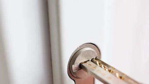 A perforated key is inserted into the keyhole of a white plastic door close-up Stock Footage 202644514