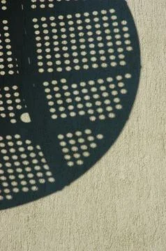 Perforated round object shadow on textured stucco wall Stock Photos