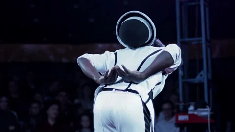 Performer juggling hat behind back on stage, audience blurred in background, Stock Footage 342231039