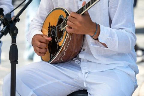 A performer skillfully strums a bouzouki while dressed in light clothing in C Stock Photos