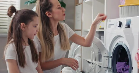 Performing clothes wash in a washing machine step by step. Woman shows daughter 動画素材 200991740