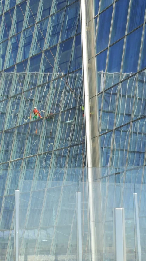 Performing Professional Window Cleaning on a Tall Skyscraper with Reflective Stock Footage 296730848