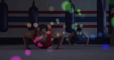 Performing pushups front man wearing red tank top on gym mat, with punching bags Stock Photos