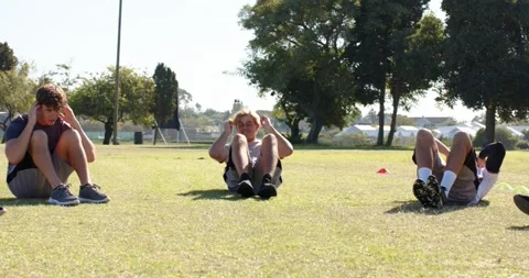 Performing sit-ups male teammates lying on grass under trees in park, training Stock Footage 344945986