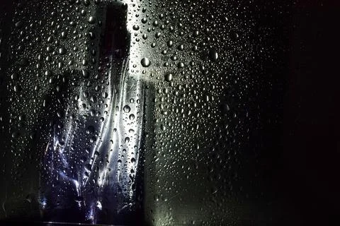 Perfume bottle on a black background through water drops Stock Photos