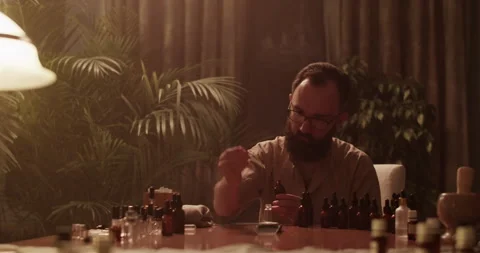 Perfumer in glasses mixing oils while creating handmade perfume Stock Footage 260986372