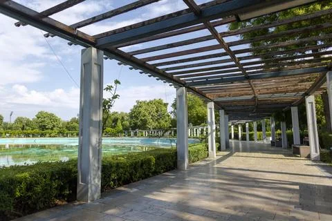 Pergola frames serene poolside: sunlit walkway beside turquoise water, lush.. Stock Photos