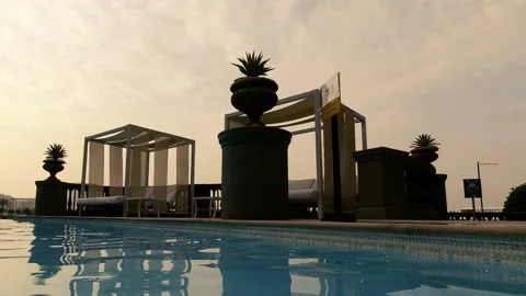 Pergola with white curtains and bed by the pool on the background of a sunset Stock Footage