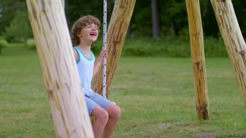 Perky cheerful boy laughs while sitting on a swing. Stock Footage 219315033