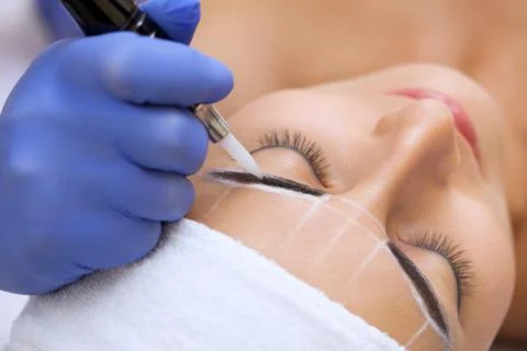 Permanent make-up for eyebrows of beautiful blonde woman in beauty salon. Stock Photos