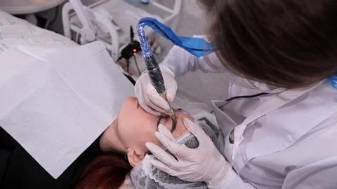 Permanent make-up master sprays paint on the eyebrow. View from above. 4K Slow Stock-Footage 106894604