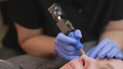 Permanent makeup artist applying pigment to eyebrows with tattooing device Stock Footage 337139591