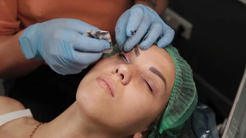 A permanent makeup artist gets a tattoo on a woman's upper eyelids. 库存影片 137543376