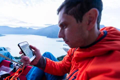 Perplex man looking at phone sitting on portaledge at sunset thinking Stock Photos