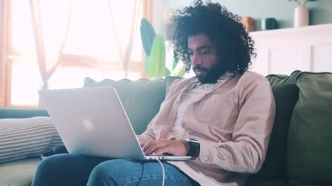 Perplexed Arabian man programmer with laptop on lap grabbing chin sits on couch Stock Footage 218939985