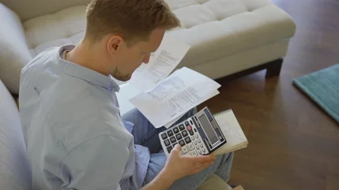 Perplexed man calculating expenses at home Stock Footage 133964573