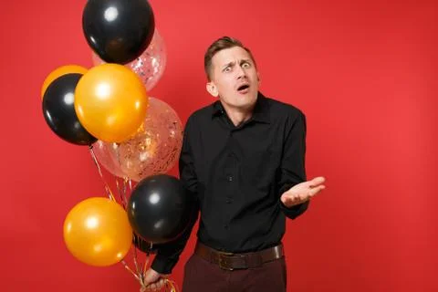Perplexed young man in black classic shirt holding air balloons, spreading hands Stock Photos