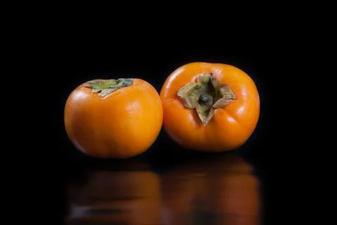 Persimmons on black reflective background Stock Photos