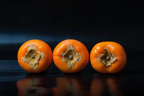 Persimmons on black reflective background Stock Photos
