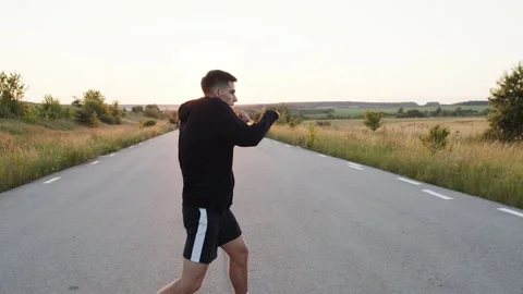 Persistent kickboxer training kicks on country road singly during sunset Stock Footage 139799611