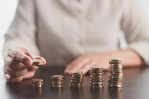 Person adding coins to rising stacks represents consistent saving, investme.. Stock Photos