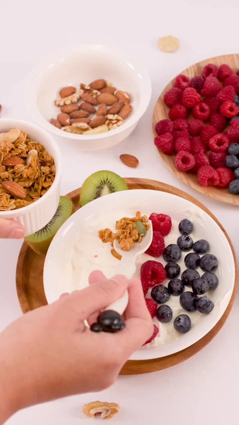Person Adding Crunchy Granola to a Fresh Greek Yogurt Breakfast Bowl Stock Footage 338051741