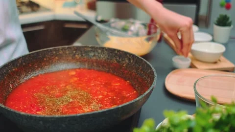 Person adding fine seasoning to tomato sauce in modern kitchen 스톡 동영상 342875286