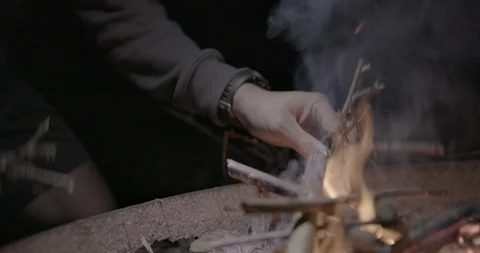Person adding firewood and blowing campfire at night Video stock 104200677