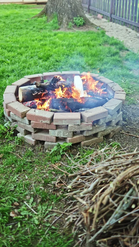 Person adding logs to a fire pit in a backyard on a cool evening with smoke Video stock 339500657