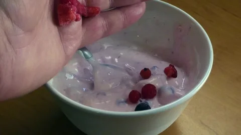 Person adding raspberries and blueberries into a bowl of yogurt for a healthy Stock Footage 337006103