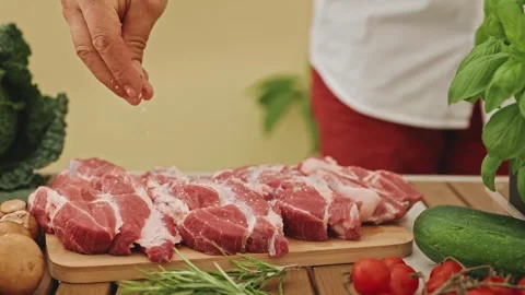 Person adding salt to cutting board with meat and vegetables, preparing food 스톡 동영상 269035080