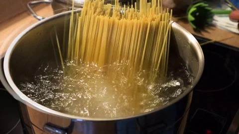 Person adding spaghetti to boiling water on a kitchen stove. Video stock 280468570