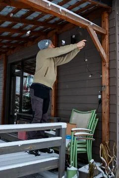 Person Adjusting String Lights on Snow Covered Wooden Terrace in Winter Stock Photos