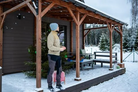 Person Adjusting String Lights on Snow Covered Wooden Terrace in Winter Photos