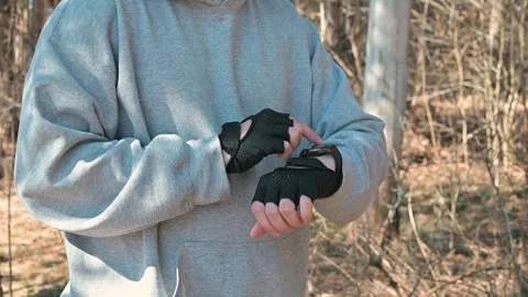 A person adjusts fingerless gloves while standing in an outdoor area surrounded Vidéo 337642986