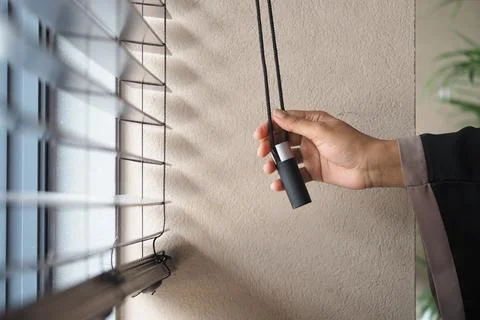 Person adjusts window blinds with a pull cord in the room Stock Photos