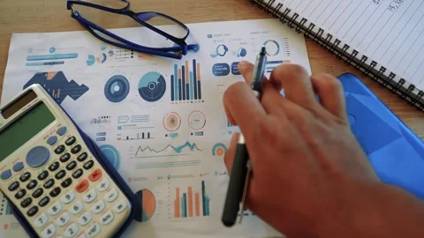 Person analyzing data charts with a calculator and pen on a desk Stock Footage 318056889