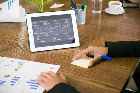 Person analyzing data on tablet with notes and charts on wooden desk Stock Photos