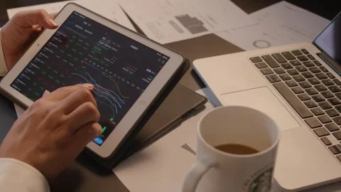 Person Analyzing Financial Charts on Tablet in Busy Office Workspace Vidéo 336552023