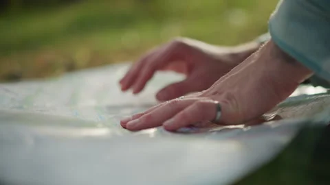Person analyzing folded map amid grassy terrain with sunlight reflections Stock Footage 333655715