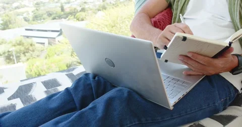 Person angling laptop forward and flipping notebook, then writing notes for work Stock Footage 341468116