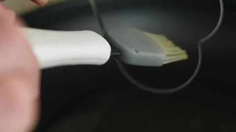 Person anoints the stainless heart shaped egg ring with oil Stock Footage 329054878