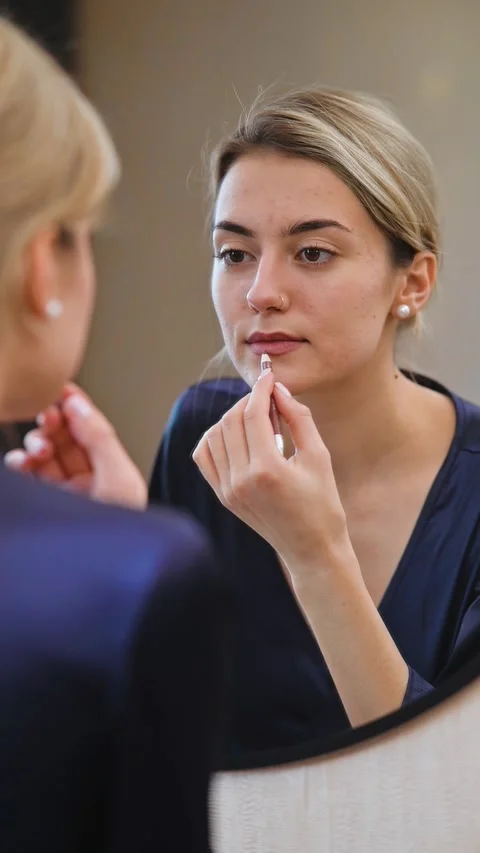 A person is applying makeup while engaged in a skincare routine in front of a Stock Footage 337555571