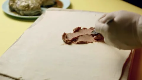 Person is applying meat pate in a thin layer on the sheet of puffy pastry Stock Footage 330288720