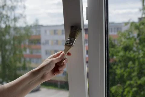 Person applying protective coating or paint on a window profile indoors. Hand Stock Photos