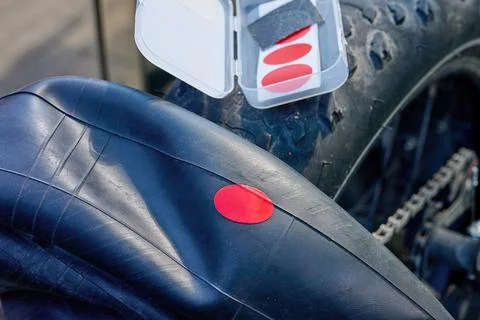 A person is applying a red patch to a bicycle tire using a repair kit on a su Stock Photos